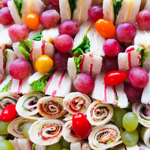 Plateau buffet comprenant des wraps, des mini sandwiches, des tomates cerises, du raisin...